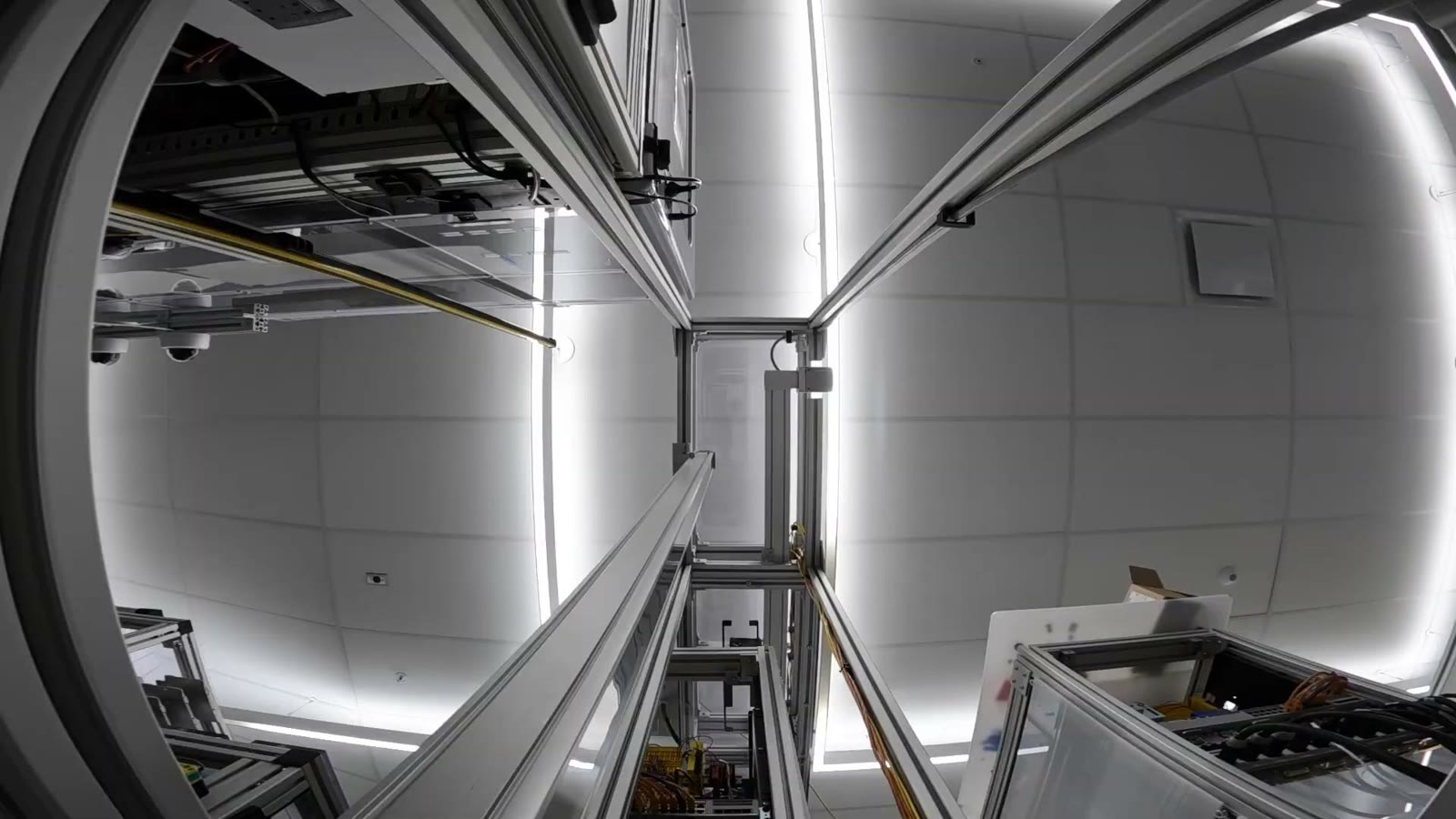 View from inside a SkySlide lift tower looking straight up, with aluminum framing rising toward the ceiling and the overhead passthrough above